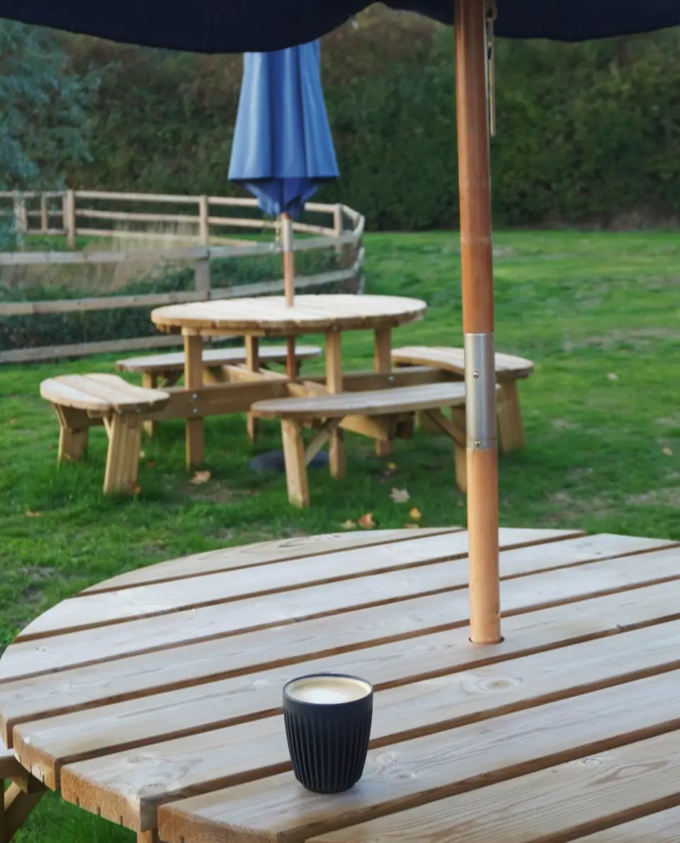 Wooden picnic tables on the grass outside Mac’s Deli in Theale, with a coffee on the table